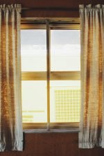Warm sunlight streaming through fabric curtains in a wooden interior setting.